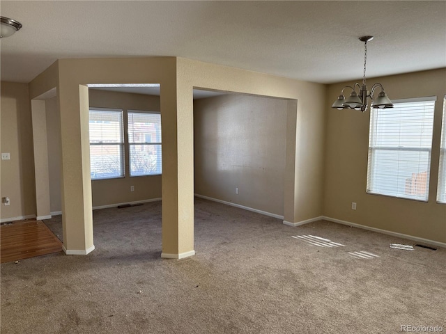 carpeted empty room featuring a chandelier