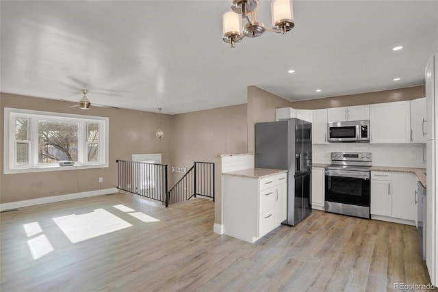 kitchen featuring ceiling fan with notable chandelier, stainless steel appliances, light hardwood / wood-style flooring, white cabinets, and hanging light fixtures