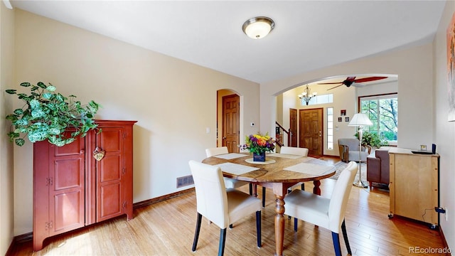dining area with arched walkways, light wood-style floors, a ceiling fan, baseboards, and a chandelier