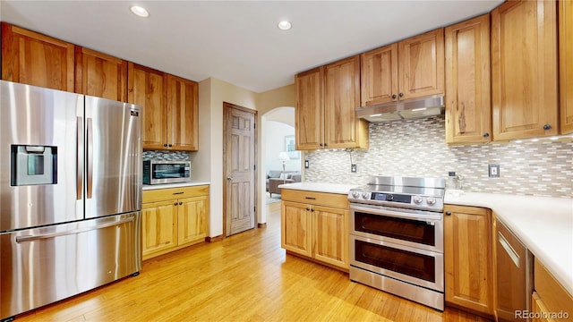 kitchen with appliances with stainless steel finishes, under cabinet range hood, arched walkways, light countertops, and recessed lighting