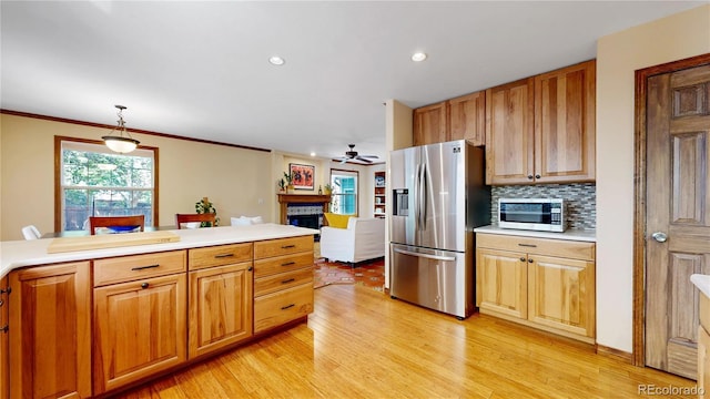kitchen with stainless steel appliances, a fireplace, light wood finished floors, a ceiling fan, and light countertops