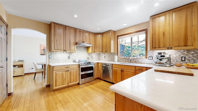 kitchen with stainless steel appliances, a sink, under cabinet range hood, light countertops, and light wood-style floors