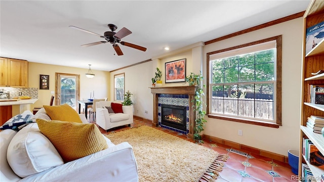 living room featuring a ceiling fan, baseboards, a glass covered fireplace, ornamental molding, and tile patterned flooring