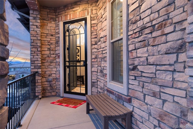 view of exterior entry featuring a balcony and stone siding