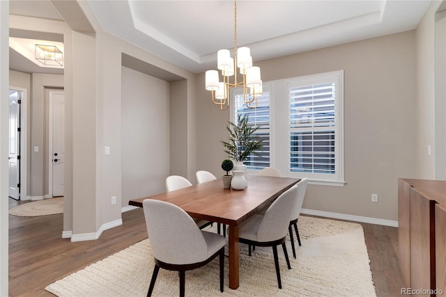 dining area featuring a tray ceiling, baseboards, and wood finished floors