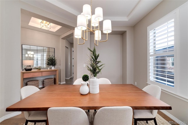 dining space featuring baseboards, wood finished floors, a raised ceiling, and an inviting chandelier