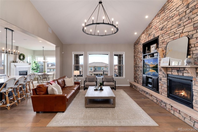 living room with baseboards, a chandelier, wood finished floors, a fireplace, and high vaulted ceiling