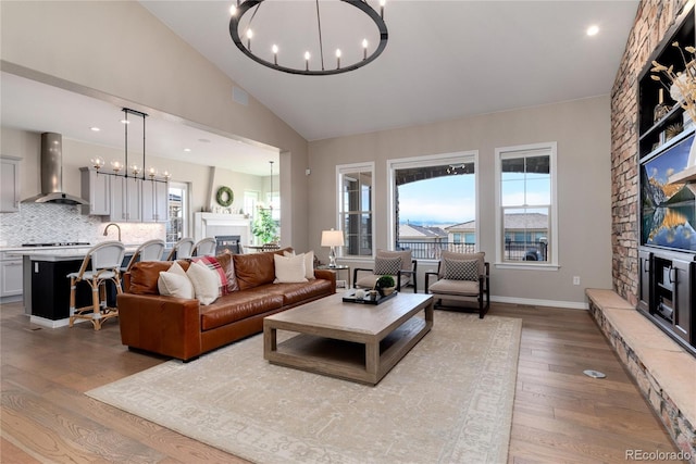 living area with a notable chandelier, a glass covered fireplace, wood finished floors, high vaulted ceiling, and baseboards