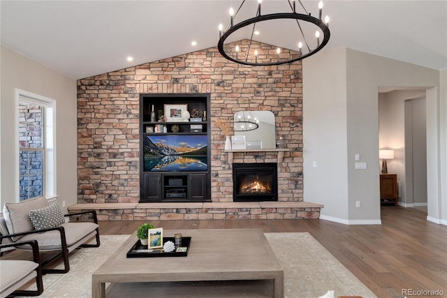 living room featuring baseboards, wood finished floors, an inviting chandelier, vaulted ceiling, and a fireplace