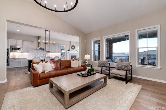 living room featuring light wood-style floors, a warm lit fireplace, a healthy amount of sunlight, and an inviting chandelier