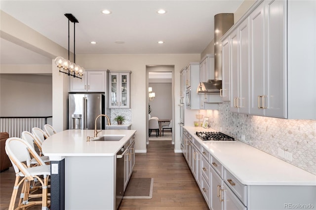 kitchen with a kitchen island with sink, stainless steel appliances, wood finished floors, a sink, and a kitchen bar