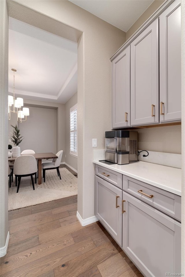 kitchen with a notable chandelier, gray cabinets, light countertops, light wood-style flooring, and baseboards