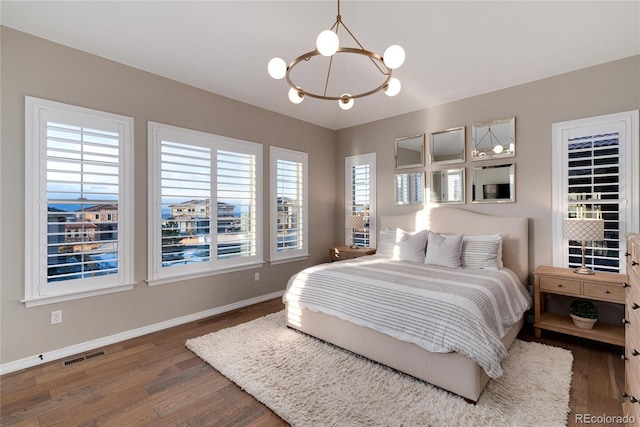 bedroom featuring visible vents, baseboards, a notable chandelier, and wood finished floors