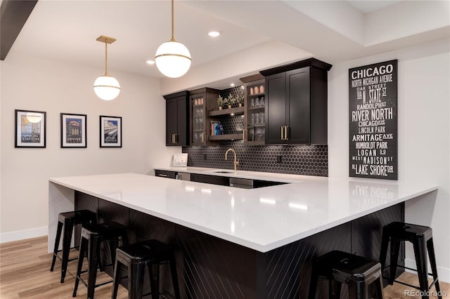 kitchen with tasteful backsplash, light countertops, glass insert cabinets, light wood-style floors, and baseboards