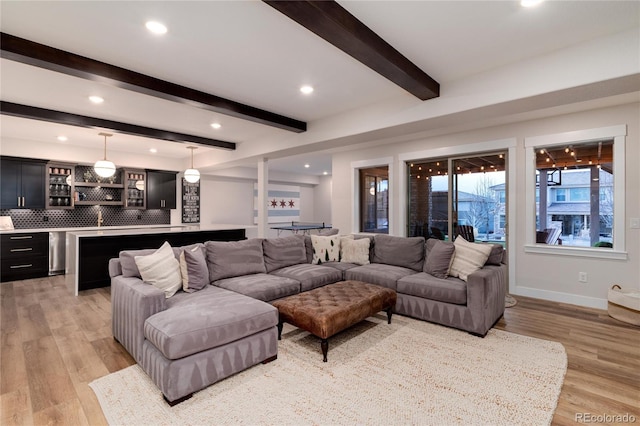 living area with wet bar, beam ceiling, light wood-style flooring, and baseboards