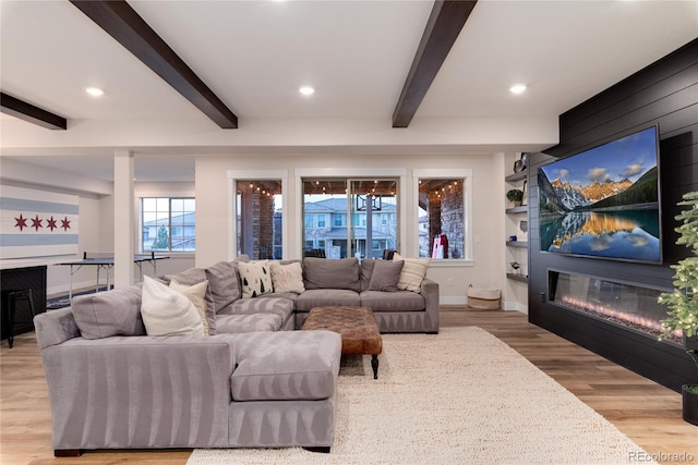 living area featuring recessed lighting, a glass covered fireplace, wood finished floors, beamed ceiling, and baseboards