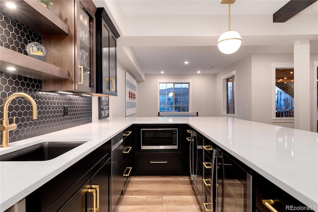 kitchen featuring light wood-style flooring, stainless steel microwave, a sink, light countertops, and backsplash