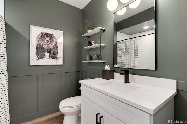 full bathroom featuring wainscoting, toilet, wood finished floors, vanity, and a decorative wall