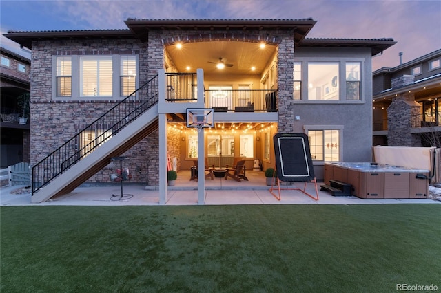 back of property at dusk featuring a patio, stairs, a lawn, stucco siding, and a hot tub