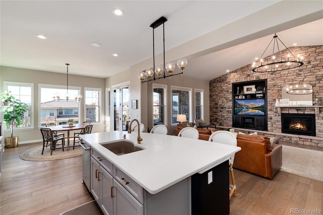 kitchen with a kitchen island with sink, a notable chandelier, a sink, and light wood finished floors