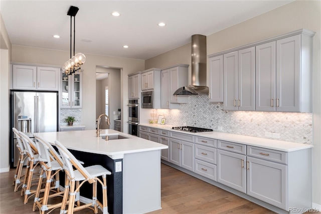 kitchen with wall chimney exhaust hood, stainless steel appliances, light wood-style floors, a kitchen bar, and a sink