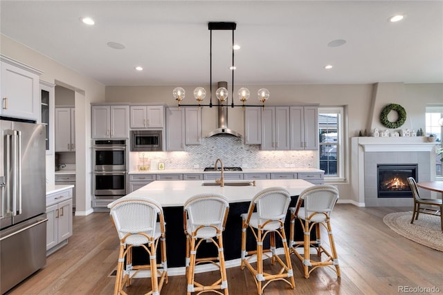 kitchen with wall chimney exhaust hood, appliances with stainless steel finishes, light countertops, and backsplash