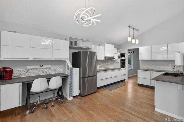 7330 Cotton Dr, Colorado Springs, CO 80923 - kitchen featuring stainless steel appliances, dark countertops, light wood-type flooring, white cabinets, and lofted ceiling