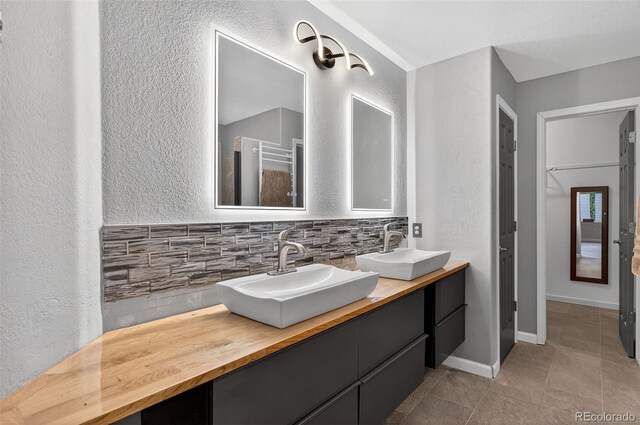 7330 Cotton Dr, Colorado Springs, CO 80923 - full bathroom with double vanity, a textured wall, decorative backsplash, tile patterned flooring, and a towel warming rack