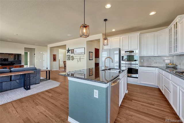 kitchen featuring wood finished floors, dark stone counters, appliances with stainless steel finishes, open floor plan, and backsplash