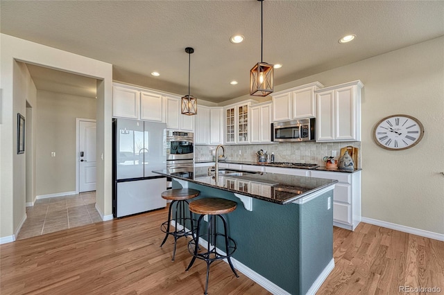 kitchen with backsplash, light wood-style flooring, appliances with stainless steel finishes, white cabinetry, and a sink