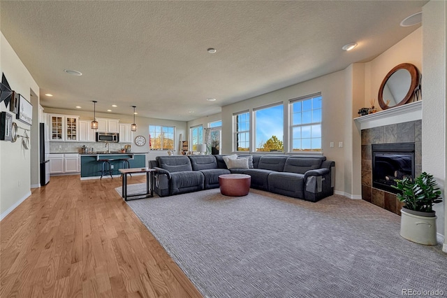 living area with baseboards, recessed lighting, a tile fireplace, a textured ceiling, and light wood-type flooring