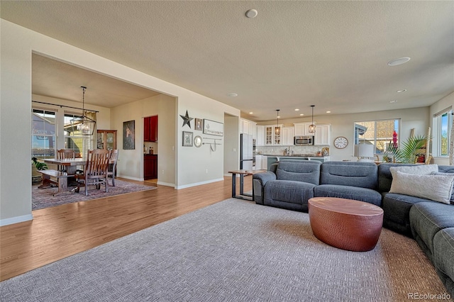 living area featuring a textured ceiling, light wood-style flooring, baseboards, and a chandelier