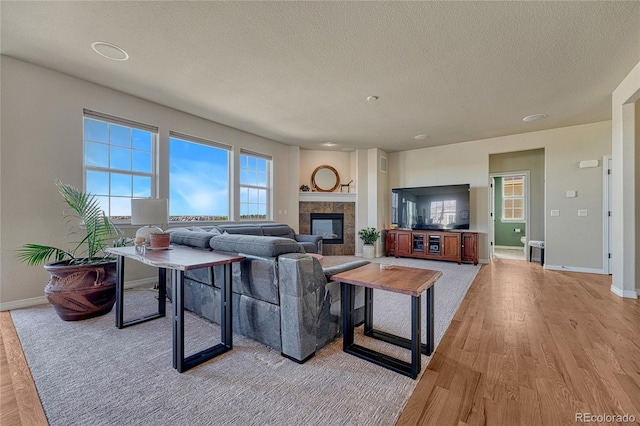 living room featuring light wood finished floors, a fireplace, a textured ceiling, and baseboards