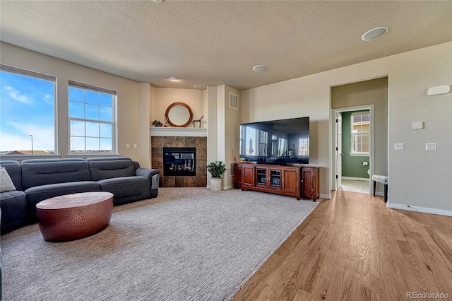 living area with light wood finished floors, visible vents, baseboards, a tiled fireplace, and a textured ceiling