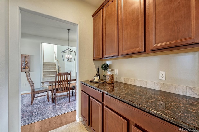 kitchen featuring brown cabinetry, a notable chandelier, dark stone counters, and baseboards