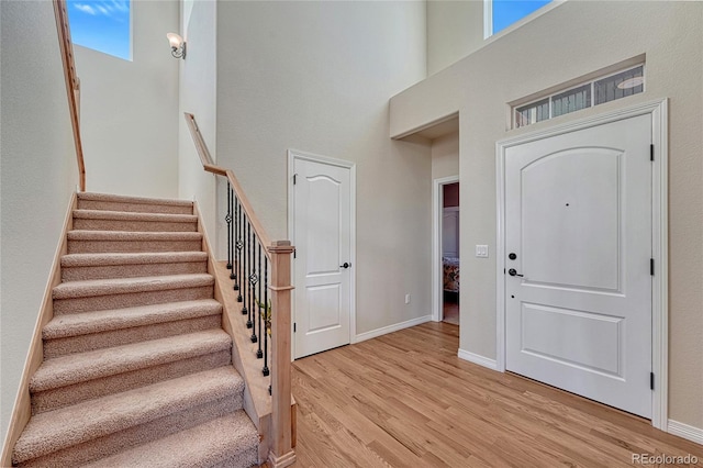 entrance foyer featuring a towering ceiling, baseboards, light wood-style flooring, and stairs