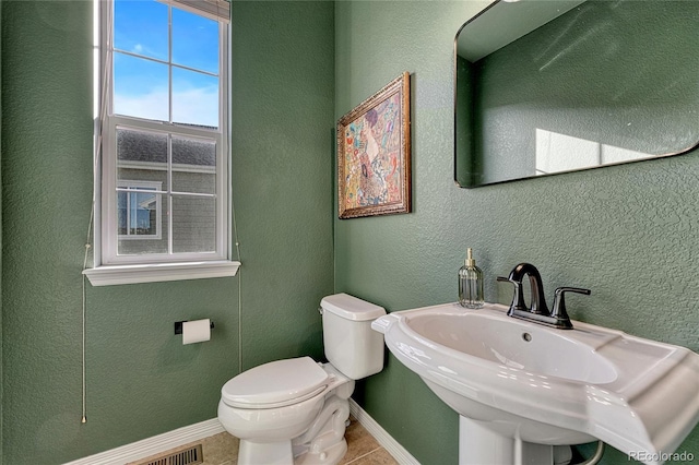 half bathroom featuring toilet, a textured wall, baseboards, and a sink