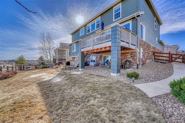 back of house with stone siding, a wooden deck, and fence