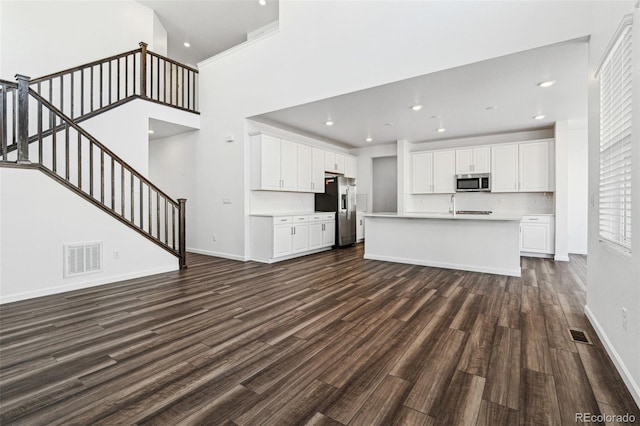 unfurnished living room featuring visible vents, baseboards, dark wood finished floors, a high ceiling, and stairs