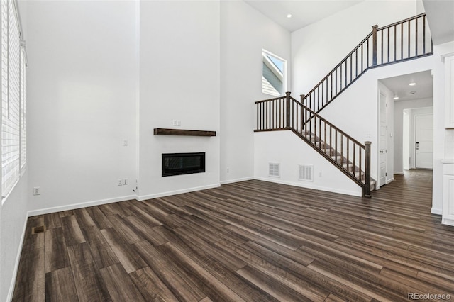 unfurnished living room featuring visible vents, dark wood-type flooring, a towering ceiling, and stairs