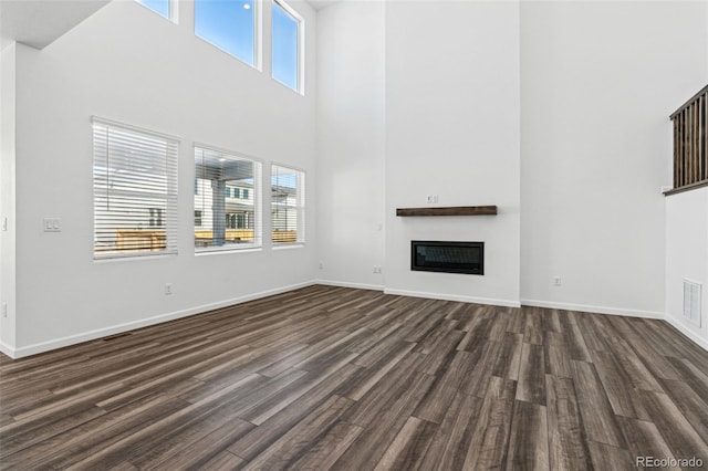 unfurnished living room with dark wood finished floors, plenty of natural light, baseboards, and a glass covered fireplace