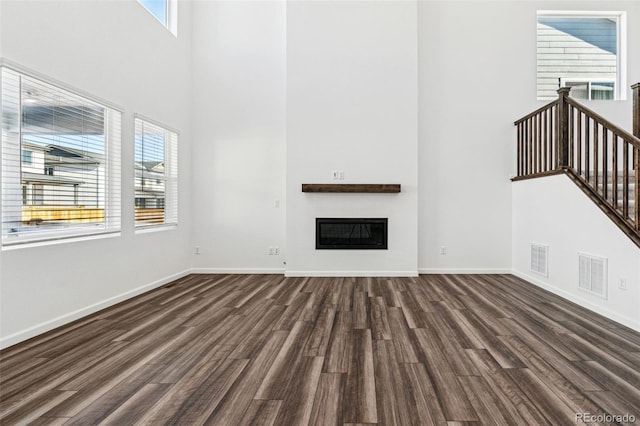 unfurnished living room with visible vents, a glass covered fireplace, dark wood-style floors, a high ceiling, and baseboards