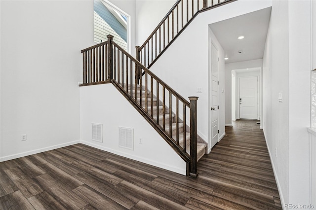staircase with a high ceiling, wood finished floors, visible vents, and baseboards
