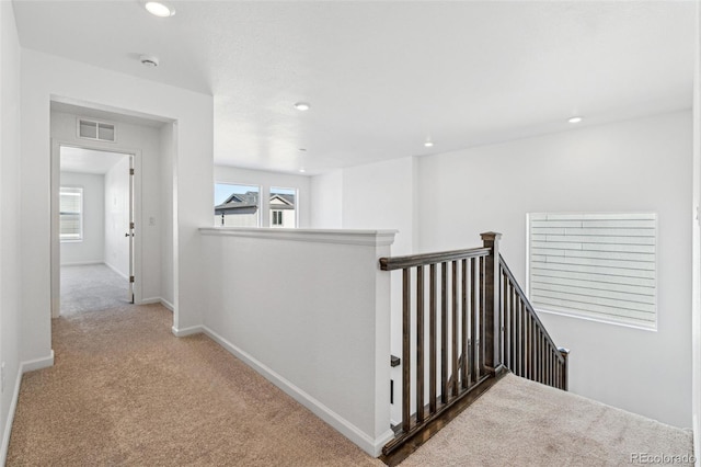 hallway with visible vents, an upstairs landing, plenty of natural light, and carpet floors