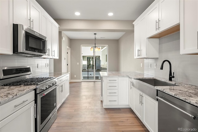 kitchen with appliances with stainless steel finishes, decorative light fixtures, sink, white cabinets, and light hardwood / wood-style flooring