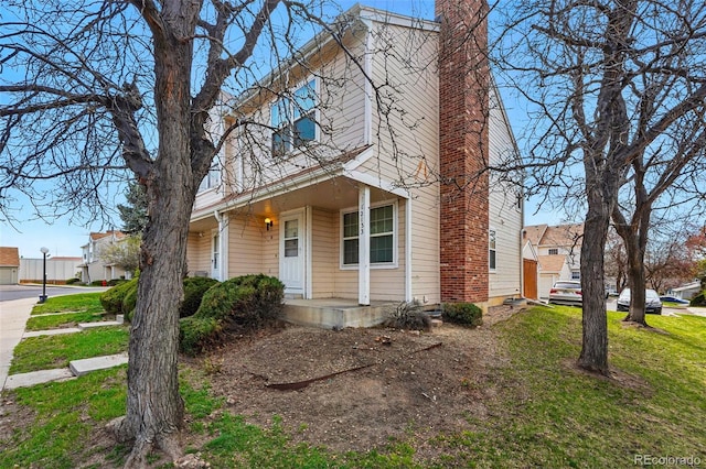 view of front of house featuring a chimney, a front lawn, and covered porch