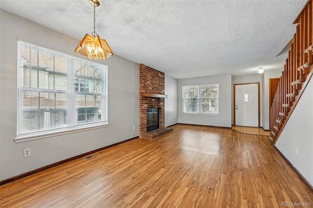 unfurnished living room with a brick fireplace, light wood finished floors, a notable chandelier, and visible vents