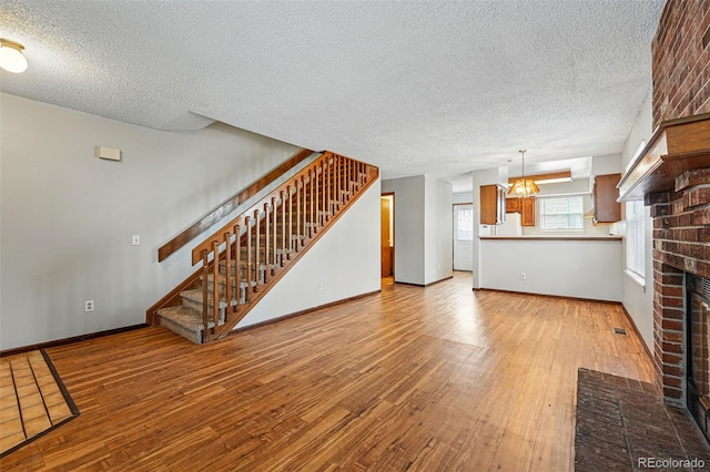 unfurnished living room with wood-type flooring, stairway, a chandelier, and a fireplace