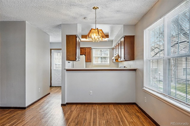 kitchen with a notable chandelier, baseboards, freestanding refrigerator, brown cabinets, and wood finished floors