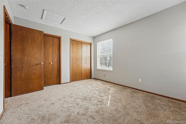 unfurnished bedroom featuring carpet, a textured ceiling, attic access, multiple closets, and baseboards